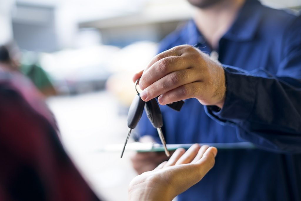 Az előző tulajdonos épp átadja a használt autó kulcsát a vásárlónak.