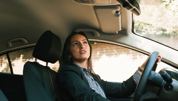 Nő ül az autó vezető ülésén, miközben az utat nézi.