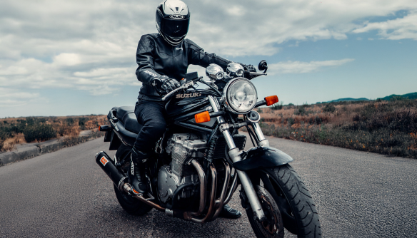 Motoros az út közepén a motoron ül, rajta tetőtől talpig fekete motoros ruha.