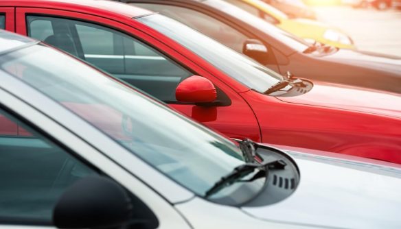 A képen különböző színű személyautók parkolnak egymás mellett egy szabadtéri parkolóban, szorosan egymáshoz rendezve. A kompozíció rendezett sorokkal és visszatükröződő felületekkel a városi közlekedés, autótulajdonlás vagy kereskedelmi járműpark hangulatát idézi.