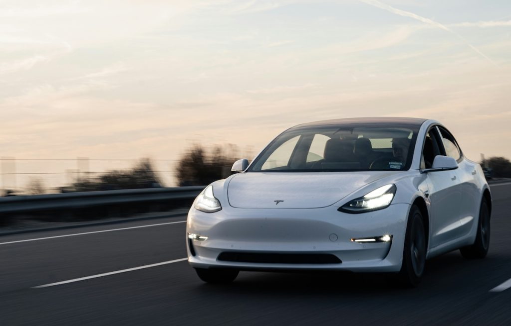 Fehér Tesla az úton, a háttérben lemenő nap fényével.