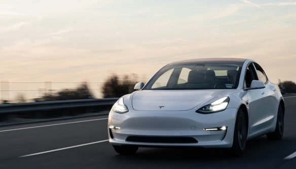 Fehér Tesla az úton, a háttérben lemenő nap fényével.