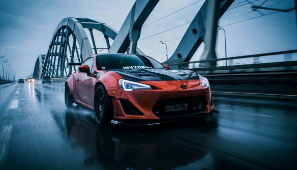 Piros Toyota sportautó esős úton, nagy sebességgel haladva egy modern acélhídon, LED fényszórókkal és sportos kialakítással.