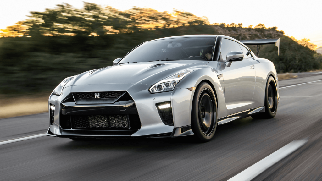 Egy modern, ezüst színű GT-R R35 száguld az úton, a háttérben elmosódott fák és a lemenő nap fénye.