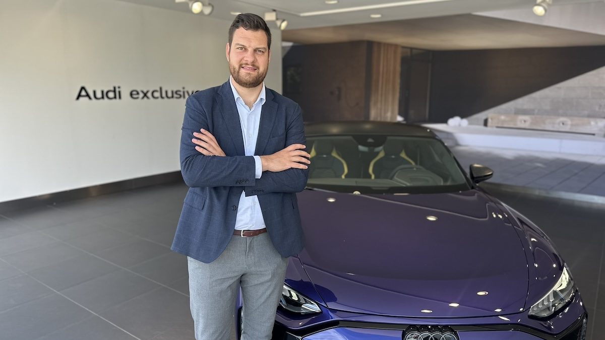 Tóth Ádám, az Audi magyarországi marketing menedzsere áll egy kék Audi mellett.