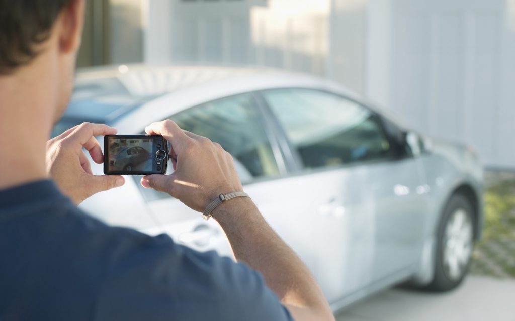 Férfi egy digitális kamerával fotót készít egy ezüst autóról. A jó fotó elengedhetetlen az autóhirdetéshez.