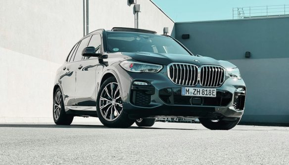 Fekete BMW SUV elölnézetből, napfényben, mögötte szürke beton épület.