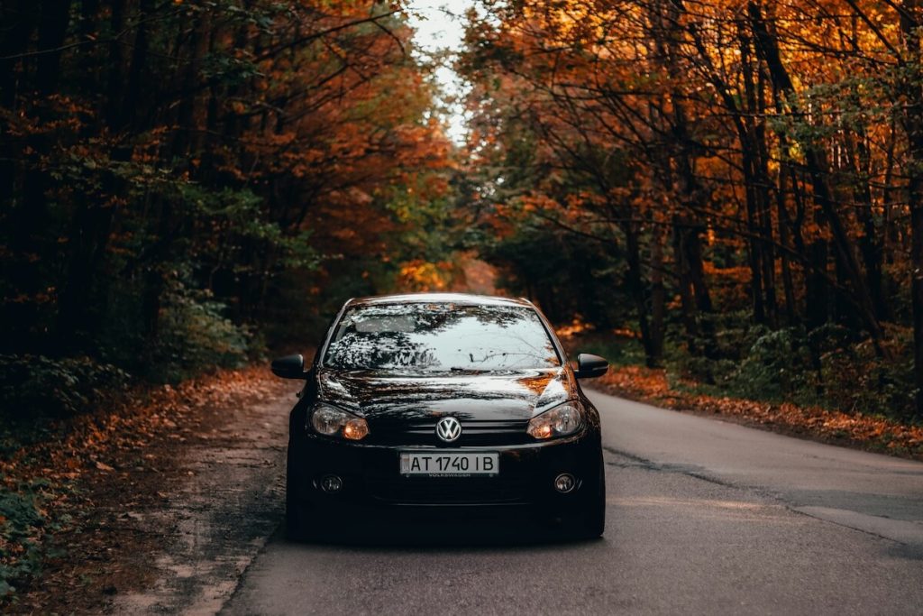 Fekete Volkswagen autó elölnézetből, őszi tájban, sárguló falevelű fákkal övezett úton. A kép a szeptemberi használtautó-piac elemzés illusztrációja.