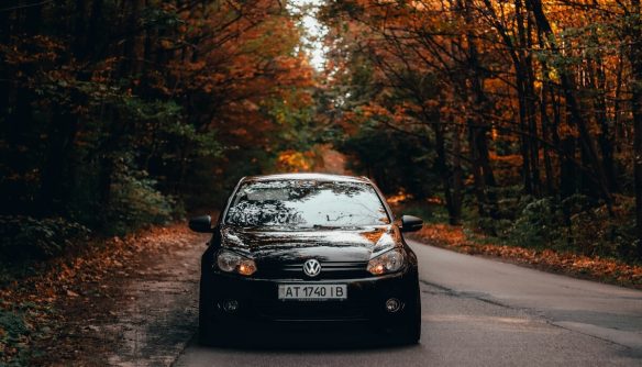Fekete Volkswagen autó elölnézetből, őszi tájban, sárguló falevelű fákkal övezett úton. A kép a szeptemberi használtautó-piac elemzés illusztrációja.