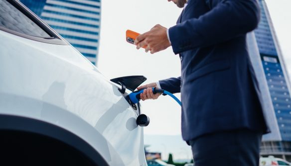 Üzletember elektromos autó töltése közben, a munkahelye melletti töltőállomáson.
