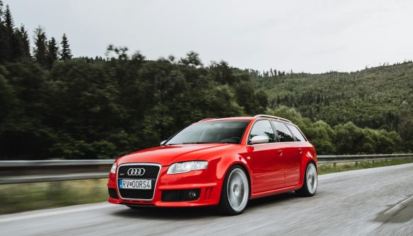 Piros Audi az autóúton, mögötte sötétzöld erdő és szürke ég.