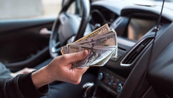 Egy férfi készpénzt nyújt a kamera felé egy autó sofőrüléséről.