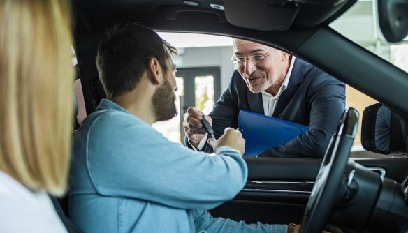 Fiatal pár az új autójukban, a kereskedő az ablakon nyújtja a kulcsokat.