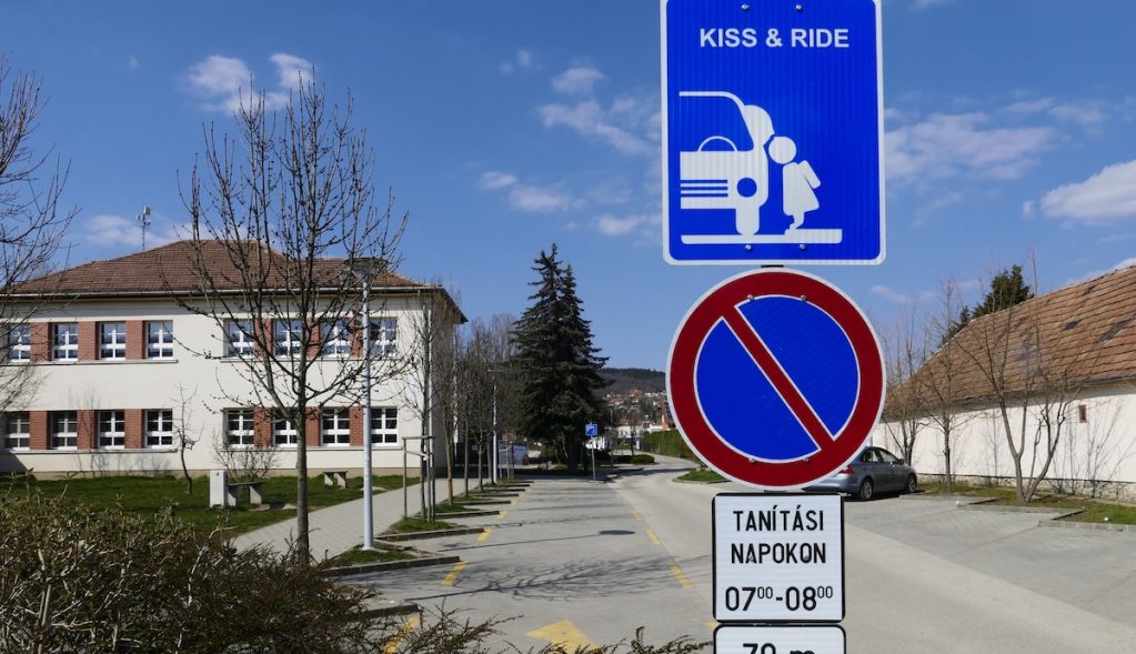 "Puszi és haladj" közlekedési tábla egy iskola mellett. A pár helyen már használt K+R táblát az új KRESZ tervezete is hivatalosan bevezeti.