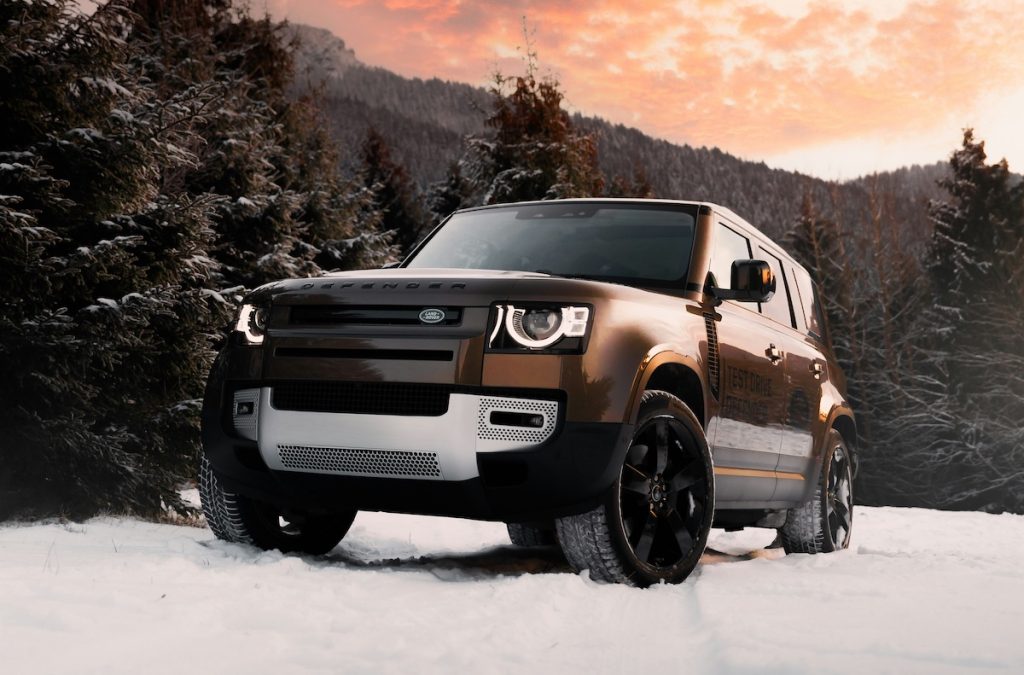 Bronz Land Rover terepjáró hóban, mögötte a lemenő nap fénye.