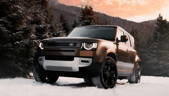 Bronz Land Rover terepjáró hóban, mögötte a lemenő nap fénye.