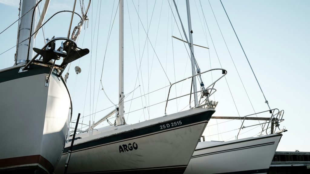 Vitorláshajók egy kikötőben, alulról fényképezve. A középső hajó oldalán látható a lajstromszám, ami a hajólevél egyik eleme is.