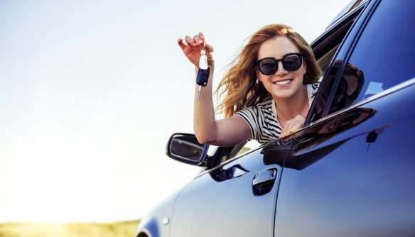 Fiatal nő hajol ki az új autója ablakán, kezében kocsikulcs.