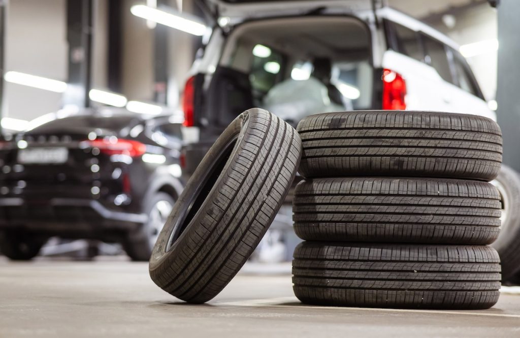 Egy garnitúra gumiabroncs, a háttérben egy használt autóval.