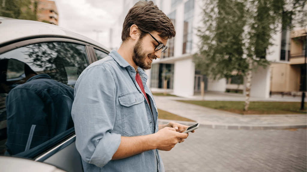 Fiatal férfi autójának támaszkodva a telefonját nézegetni.