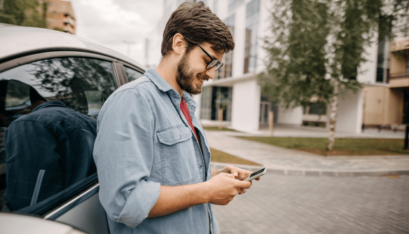 Fiatal férfi autójának támaszkodva a telefonját nézegetni.