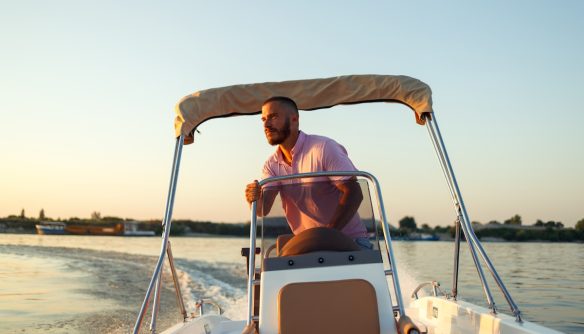 Fiatal férfi motorcsónakot vezet, a háttérben naplementével.