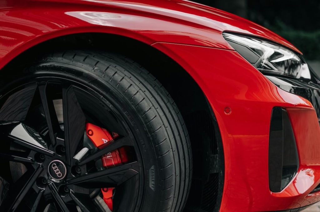 Piros sportos Audi elektromos autó első kereke és sárvédője közelről, fekete könnyűfém felnivel és piros féknyereggel. A kép az EV-specifikus gumi jellemzőit illusztrálja.