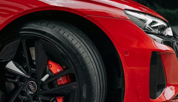 Piros sportos Audi elektromos autó első kereke és sárvédője közelről, fekete könnyűfém felnivel és piros féknyereggel. A kép az EV-specifikus gumi jellemzőit illusztrálja.