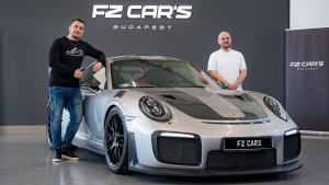 Egy szürke Porsche GT2RS az FZ Cars sajtófala előtt, mellette Lőcsei Dániel és a kereskedés értékesítője.