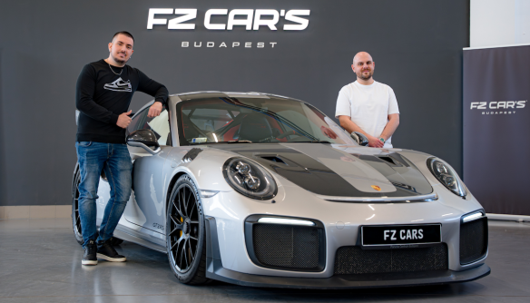 Egy szürke Porsche GT2RS az FZ Cars sajtófala előtt, mellette Lőcsei Dániel és a kereskedés értékesítője.