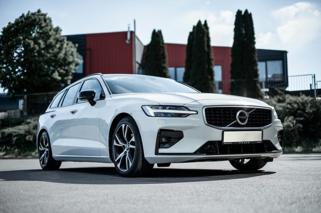 Fehér Volvo V60 parkol egy épület és fák előtt