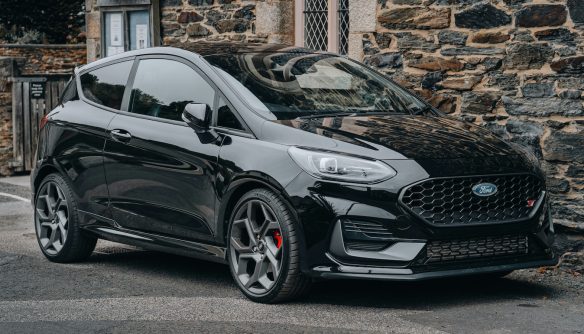 Fekete Ford parkol egy kőfal előtt