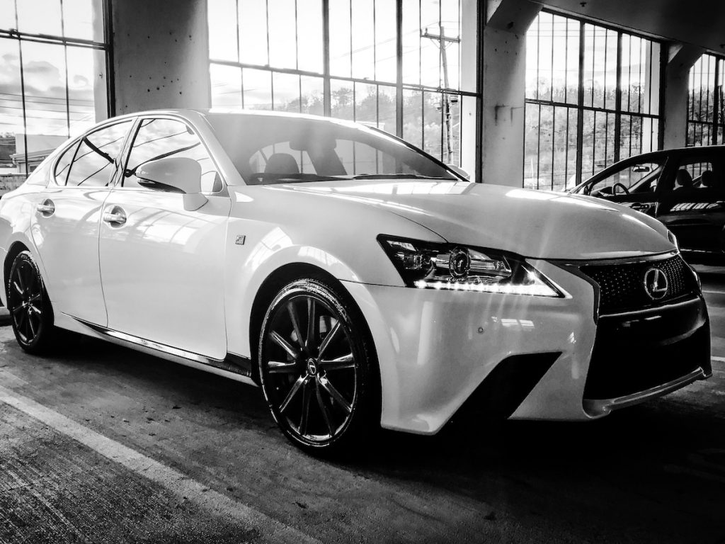 Fekete-fehér fotó egy fehér Lexus szedánról.