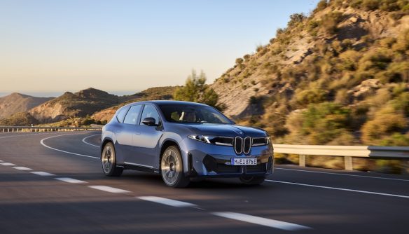 Egy új BMW ix3 50x szeli az utakat. Mögötte hegyoldal és kék ég.
